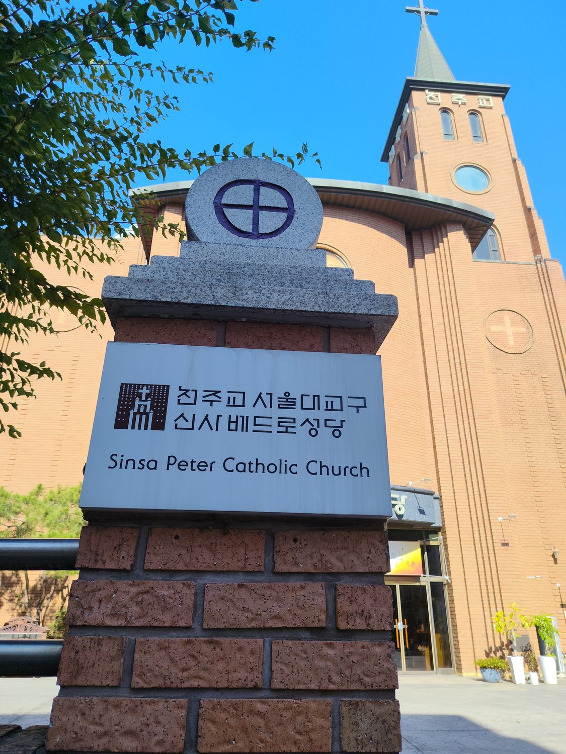Schild der katholischen Sinsa-Peter-Kirche in Seoul vor dem Backsteinturm der Kirche