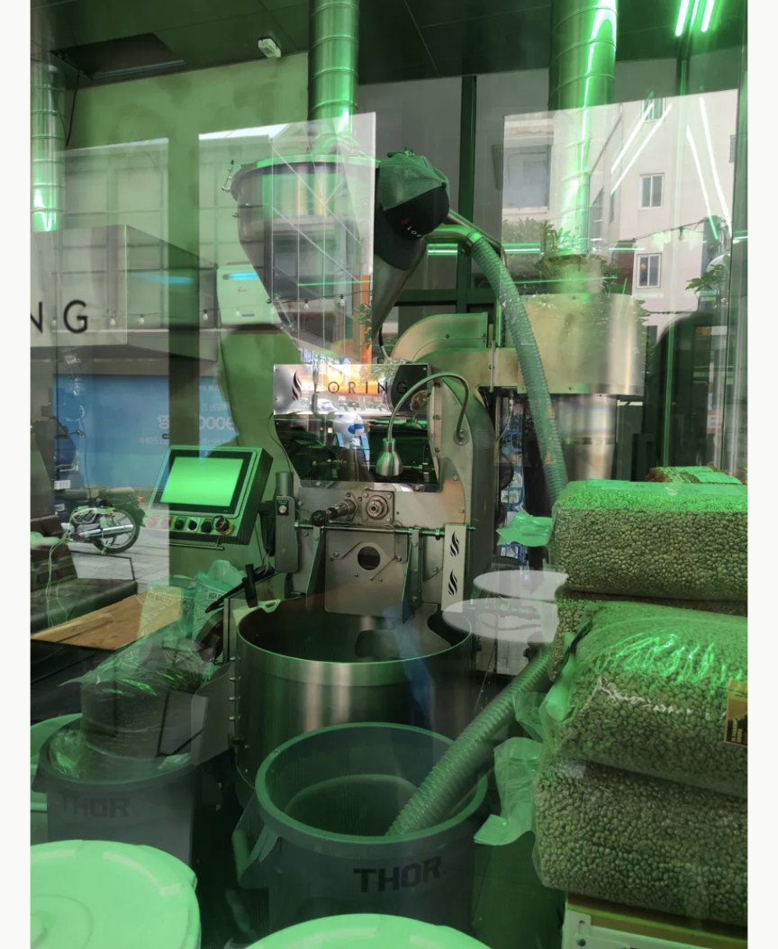 Kaffeeröstmaschine hinter Glas, daneben Säcke mit grünen Rohkaffeebohnen in einer koreanischen Rösterei