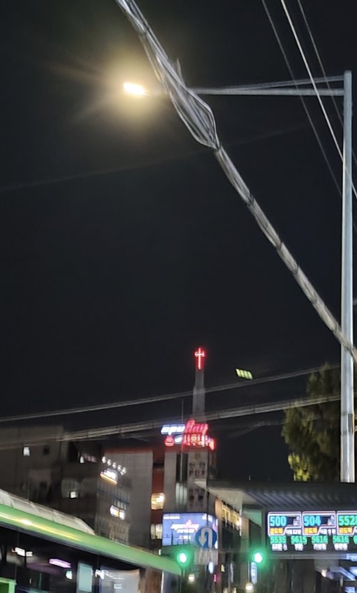 Rot leuchtendes Neon-Kreuz einer Kirche bei Nacht über den Dächern und Lichtern eines Viertels in Seoul