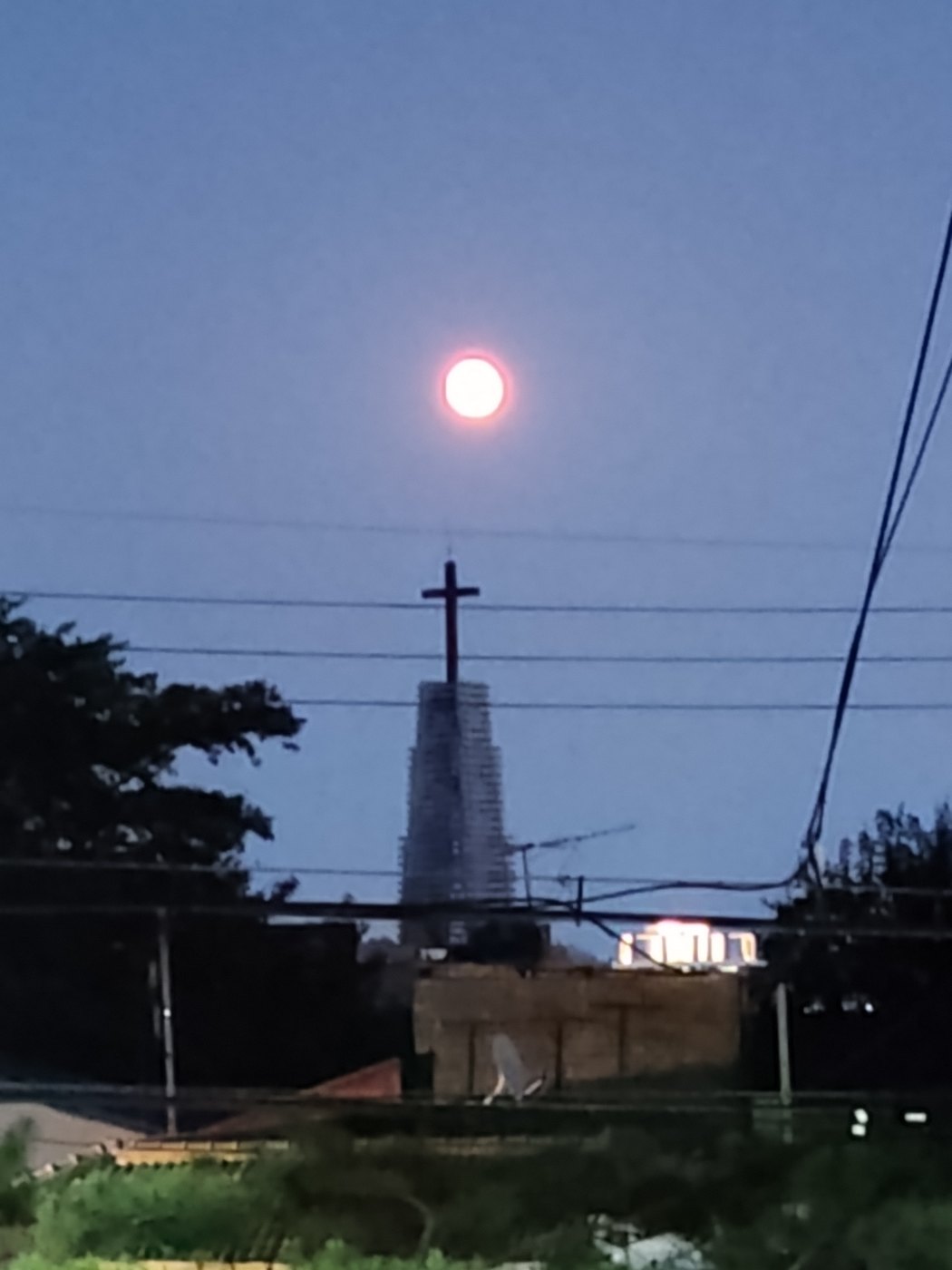 Beleuchtetes Kirchenkreuz auf einem schmalen Turm unter dem aufgehenden Vollmond über einem Viertel in Seoul