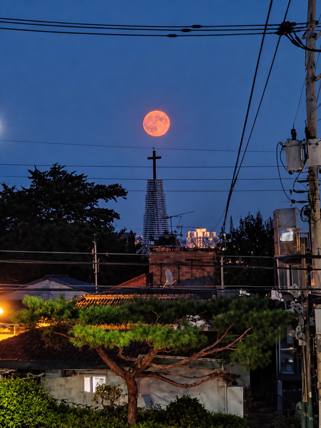 Oranger Vollmond steigt über den Dächern eines Seouler Viertels hinter einem Kirchturm auf