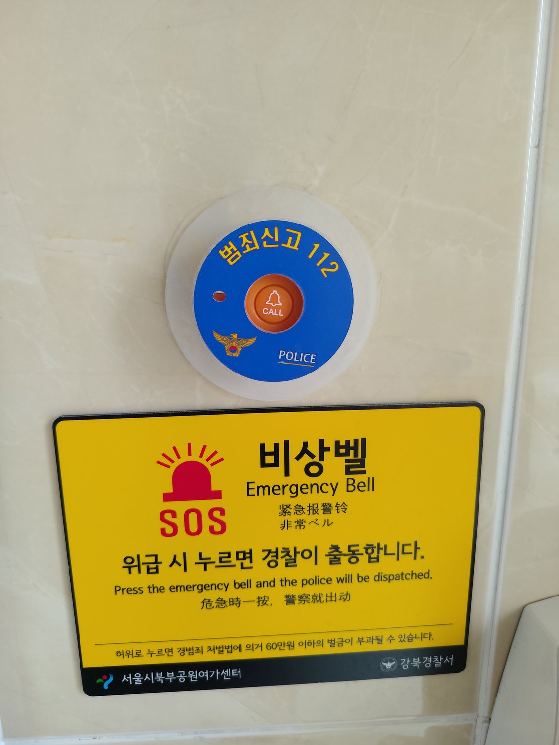 Gelber Notfallknopf „Emergency Bell / 비상벨“ mit Polizei-Alarmknopf auf einer öffentlichen Toilette