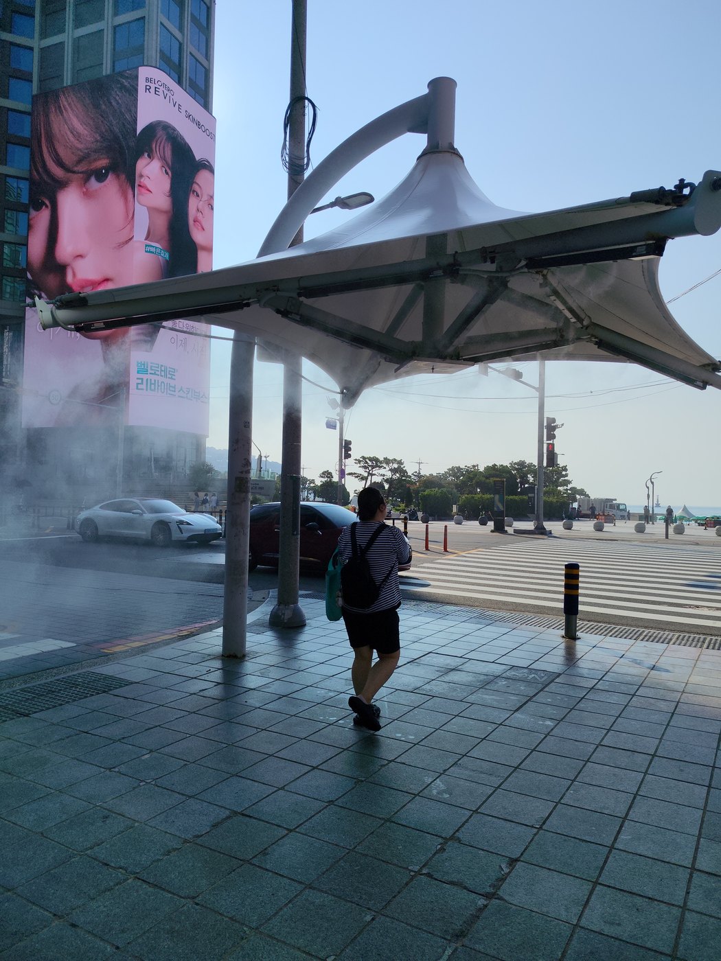 Kühlender Wassernebel unter einer Überdachung an einer Kreuzung in Korea, eine Person läuft hindurch